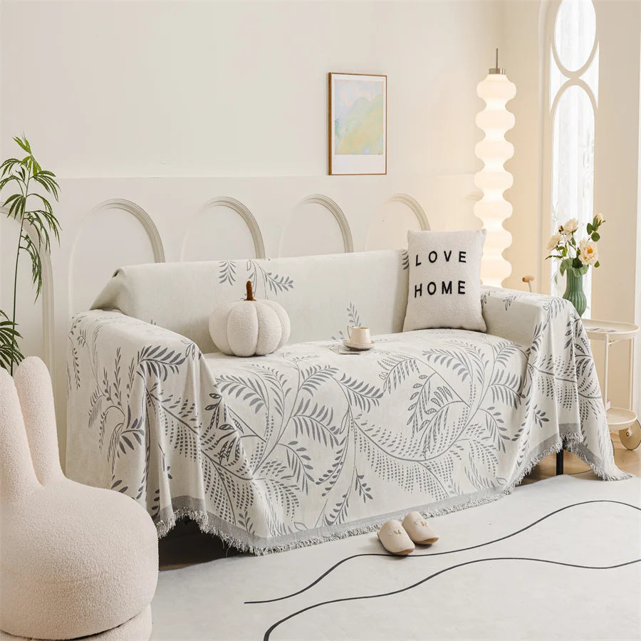 Cozy living room with a white sofa draped with a leaf-patterned throw blanket, a pumpkin, and a 'Love Home' pillow.