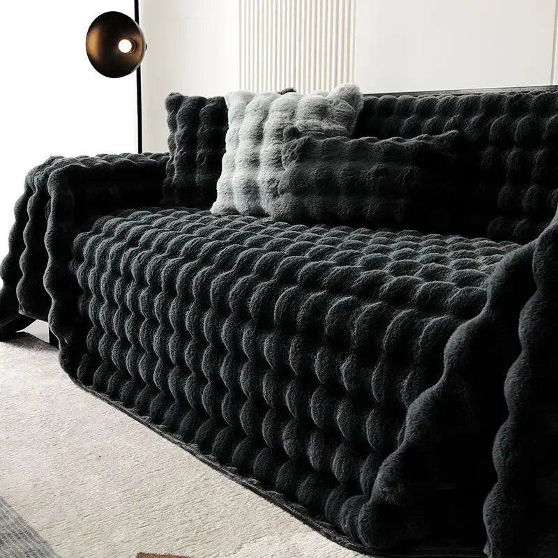 Black plush faux rabbit bubble blanket draped over a sofa with decorative pillows in a modern living room.