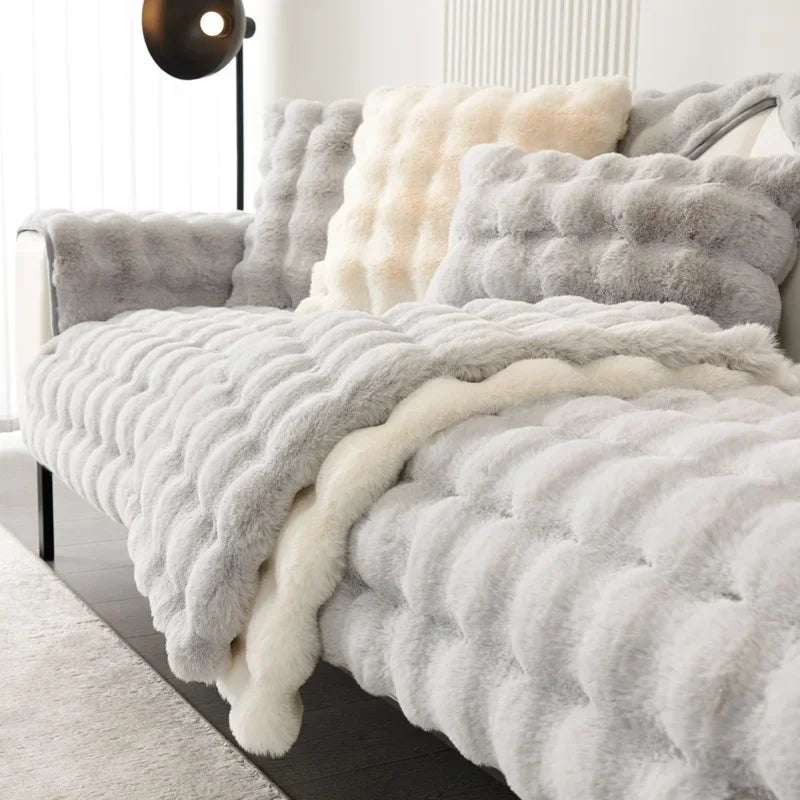 Gray and white textured plush soft blanket draped over a sofa with pillows in a cozy living room.