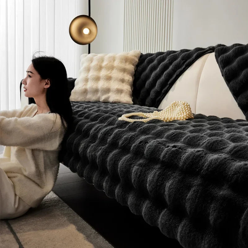 Woman sitting on the floor next to a sofa with a black plush soft textured blanket and pillows.