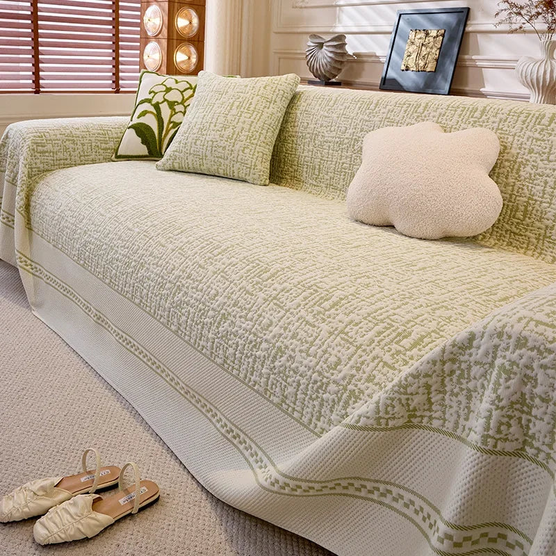 Green and beige patterned sofa cover on a couch with decorative pillows in a living room setting.