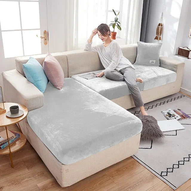 Woman sitting on a beige sectional sofa with a grey cover over one seat, in a bright living room.