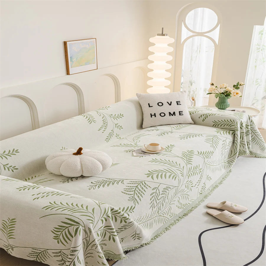 Bed with green leaf patterned blanket and 'Love Home' pillow in a bright bedroom.