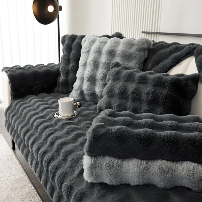 Gray textured plush soft blanket draped over a sofa with a cup on a small table.