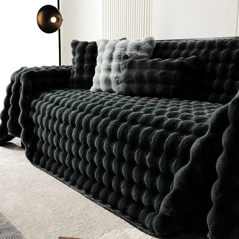 Dark grey plush faux rabbit bubble blanket draped over a sofa with decorative pillows in a modern living room.