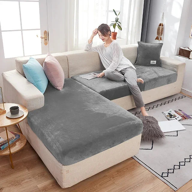 Woman sitting on a sectional sofa with grey and beige covers in a bright living room.