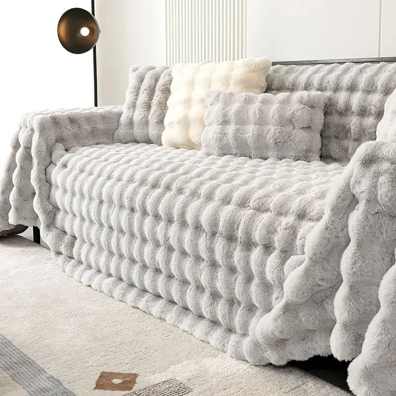 Grey fluffy blanket draped over a sofa in a room with a light-colored rug.