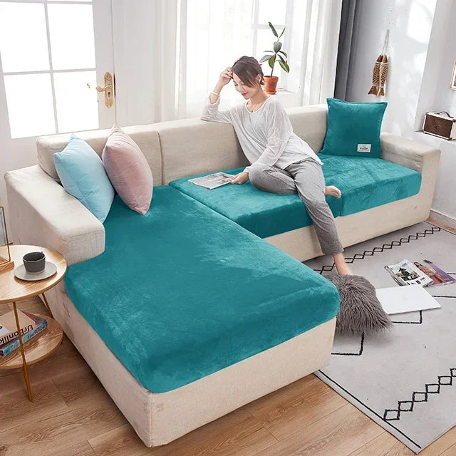 Woman sitting on a sectional sofa with teal cushions in a bright living room.